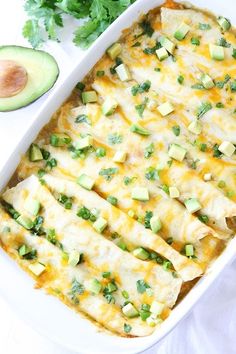 an enchilada casserole in a white dish with avocado on the side