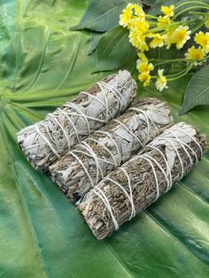 three bundles of white sage sitting on top of a green leaf covered ground next to yellow flowers