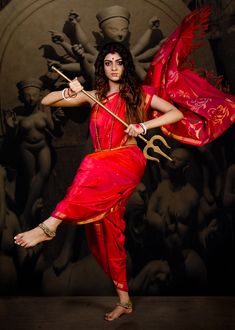 a woman dressed in red holding a staff and posing for the camera with her arms outstretched