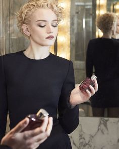 a woman in a black dress is holding a bottle and looking at her cell phone