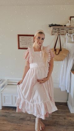 a pregnant woman in a pink dress standing next to a white wall and wooden floor