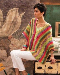 a woman sitting on top of a wooden box wearing a multicolored crocheted sweater