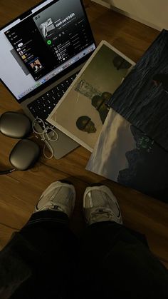 an open laptop computer sitting on top of a wooden desk next to a pair of shoes