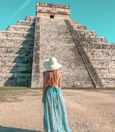 a woman standing in front of an ancient pyramid wearing a white hat and blue dress