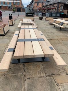 several wooden benches lined up on the side of a road in front of brick buildings