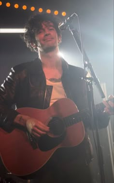 a man holding a guitar while standing in front of a microphone