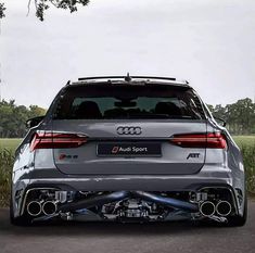 the rear end of an audi sport car parked in front of some grass and trees