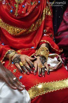 a woman in red and gold is sitting down with her hands on her chest,