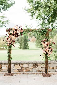 an outdoor ceremony setup with flowers and greenery on the side of the aisle, in front of a stone wall