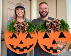 a man and woman holding up two pumpkins