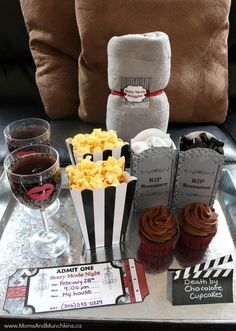 a tray topped with cupcakes and popcorn next to two wine glasses on a table