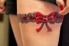 a woman with a tattoo on her thigh that has a red bow and ribbon around it