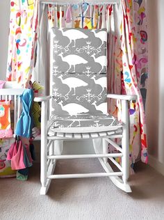 a white rocking chair sitting in front of a window with colorful curtains and drapes