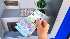 a person holding money in front of an atm machine that is open and showing the new 50 euros bill