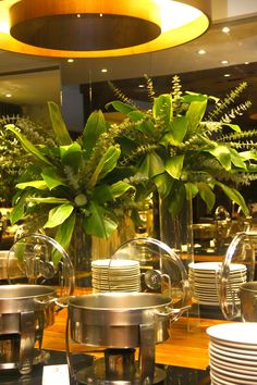 there are many plates and cups on the table with plants in vases next to them