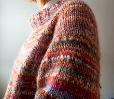 an older woman wearing a multicolored knitted sweater looking out the window with her hands in her pockets