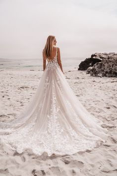 a woman standing on top of a sandy beach next to the ocean wearing a wedding dress