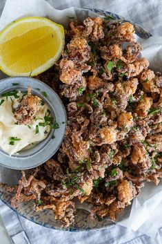 a plate filled with fried food next to a bowl of mayonnaise and lemon wedges