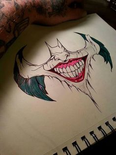 a person with tattoos on their arm holding a notebook and smiling at the camera while wearing a joker mask