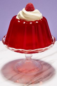 a red cake with white frosting and a raspberry on top sits in a glass dish