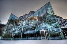 a glass building with mountains in the back ground and snow on the ground behind it