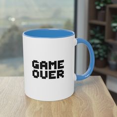 a blue and white game over coffee mug sitting on a table next to a window