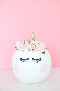 a white pumpkin decorated with pink flowers and a unicorn's face painted on it