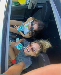 two young women sitting in the back seat of a car drinking water from plastic bottles