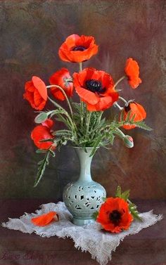 red flowers in a green vase on a lace doily with a brown background,