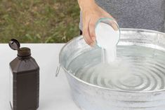 a person is pouring water into a metal bucket with a bottle on the table next to it