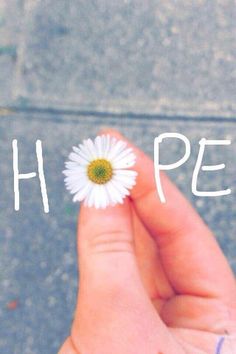 a person's hand holding a flower with the word hope written on it in front of them