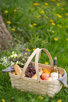 a picnic basket with bread, fruit and wine on the grass in front of a tree