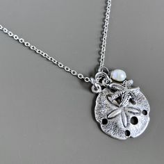 Small Sand Dollar Necklace - This is a smaller version of my other Sand Dollar necklace. The Sand Dollar is accented with a a Silver Pewter Starfish and White Freshwater Pearl. The Sand Dollar is approximately 17mm (slightly smaller than an US dime) and has a hollow back. Stainless Steel Chain For other Sand Dollar Necklaces: https://www.etsy.com/shop/mcstoneworks?search_query=sand+dollar+necklace Beachy Silver Strand Jewelry, Adjustable Silver Strand Necklace, Silver Strand Necklace For Vacation, Silver Starfish Jewelry For Vacation, Silver Jewelry With Starfish Charm For The Beach, Silver Charm Necklaces For Beach, Silver Charm Necklace For Beach, Adjustable Silver Charm Necklace For Beach, Adjustable Silver Charm Necklace For The Beach