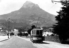 a black and white photo of a trolley car on the road in front of a mountain