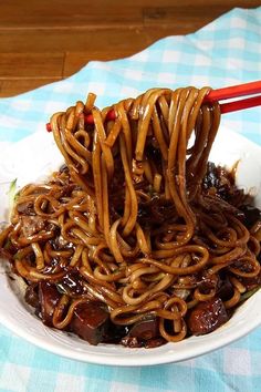 a white bowl filled with noodles and meat on top of a blue checkered table cloth