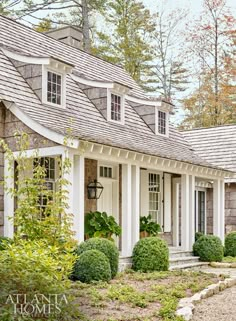 a house with white trim and shingles on the roof, surrounded by green shrubs