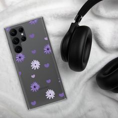 a phone case with purple and white flowers on it, next to headphones laying on a blanket