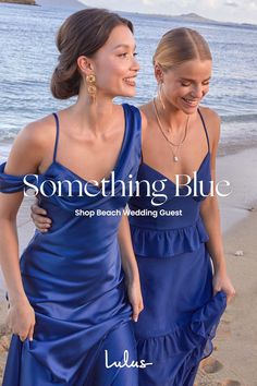 two women in blue dresses walking on the beach with text something blue shop beach wedding guest