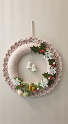 a crocheted wreath hanging on the wall with bells and holly decorations around it