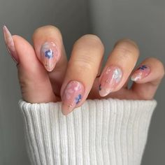 a woman's hands with pink and blue nail polishes on their nails, holding a white sweater