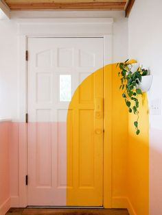 a yellow door with pink and white walls in a hallway next to a potted plant