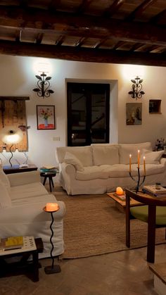 a living room filled with white furniture and lots of candles on the table in front of it