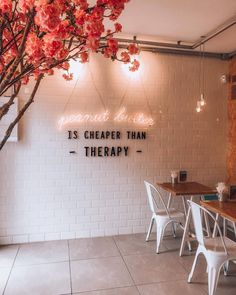 the interior of a restaurant with white chairs and wooden tables in front of a brick wall that reads'is cheaper than therapy '