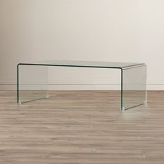 a clear glass table sitting on top of a hard wood floor next to a white wall