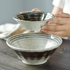 a person holding a bowl on top of a wooden table in front of another bowl