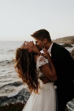 a bride and groom kissing in front of the ocean