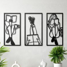 three black and white art pieces hanging on a wall next to potted palm tree