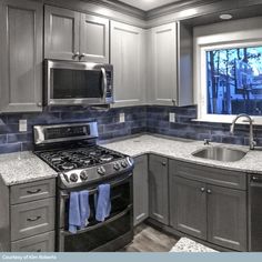 a kitchen with gray cabinets and granite counter tops, stainless steel appliances and an open window