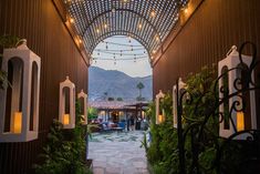 an open walkway with lights hanging from it's ceiling and potted plants on either side