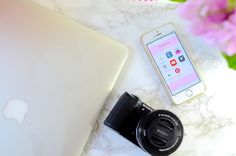 an iphone, camera and laptop sitting on a marble counter top next to pink flowers